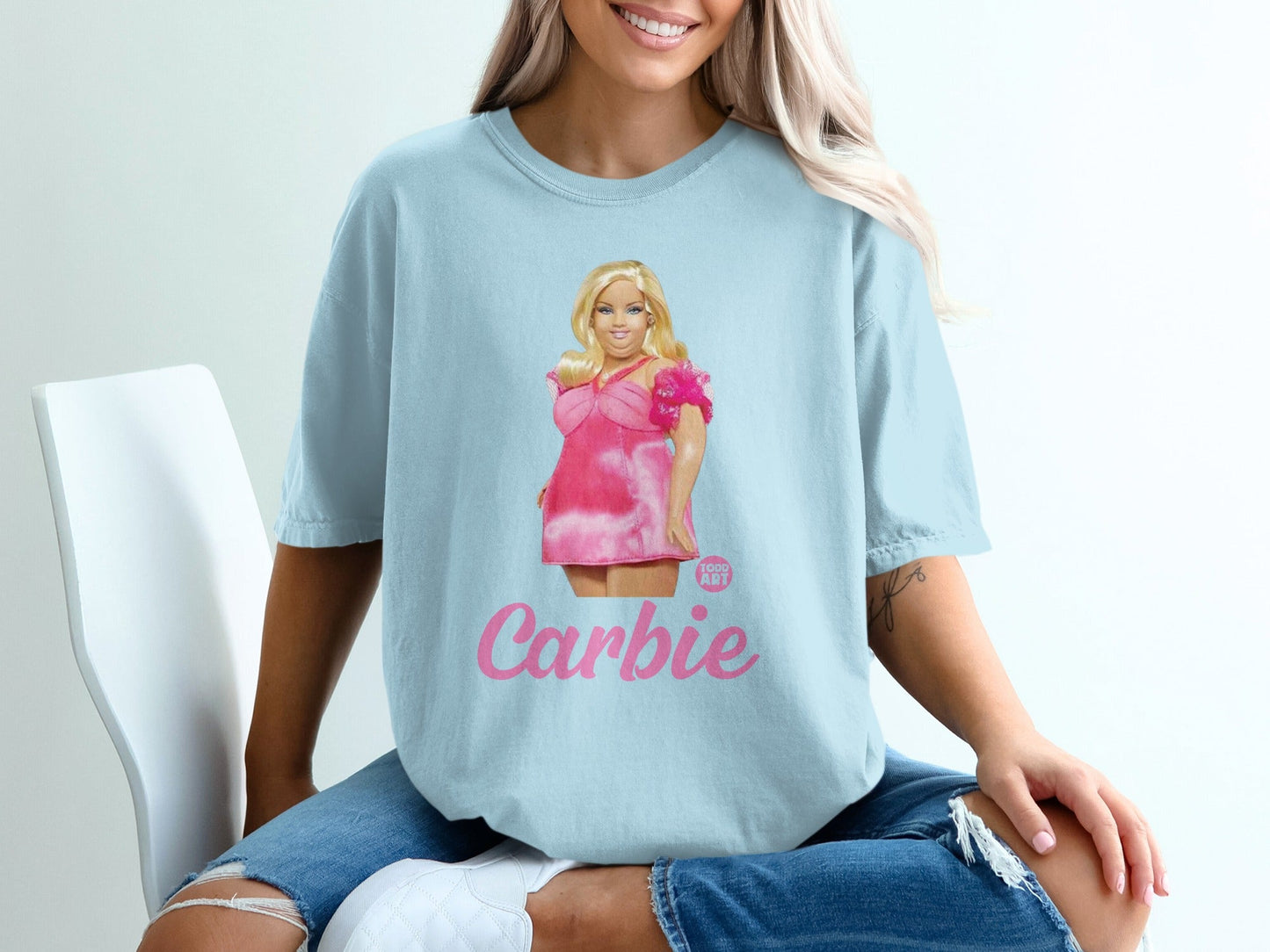 Light blue t-shirt with "Carbie" graphic of a blonde woman in a pink dress.