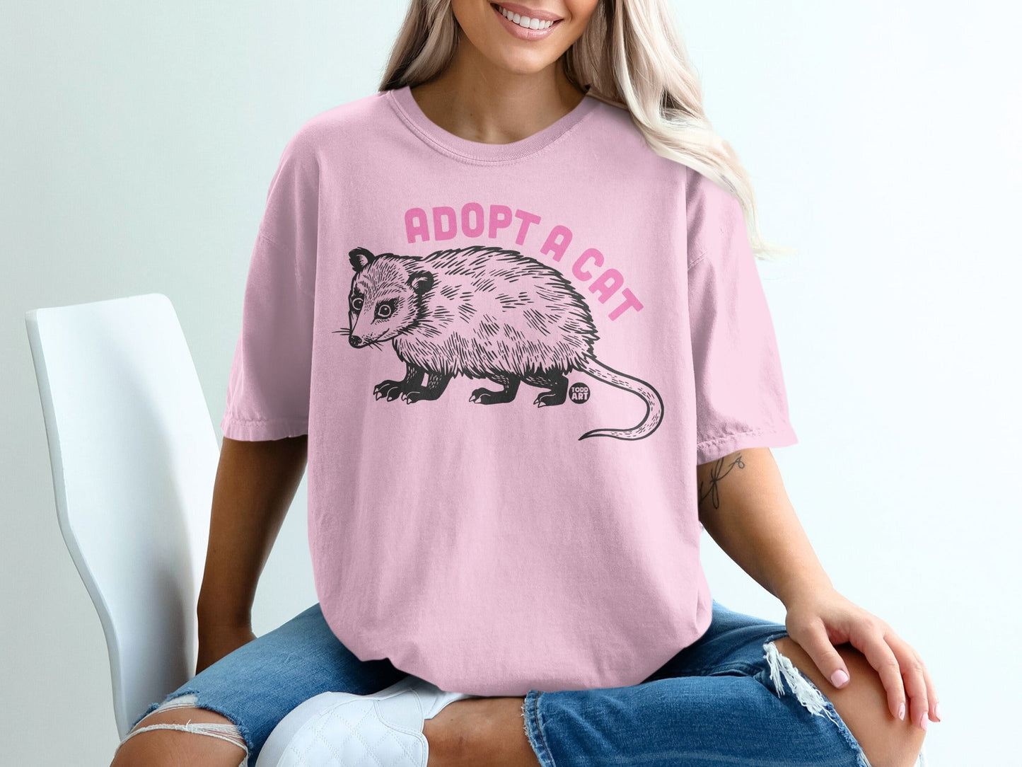 Pink t-shirt with "ADOPT A CAT" text and opossum graphic.