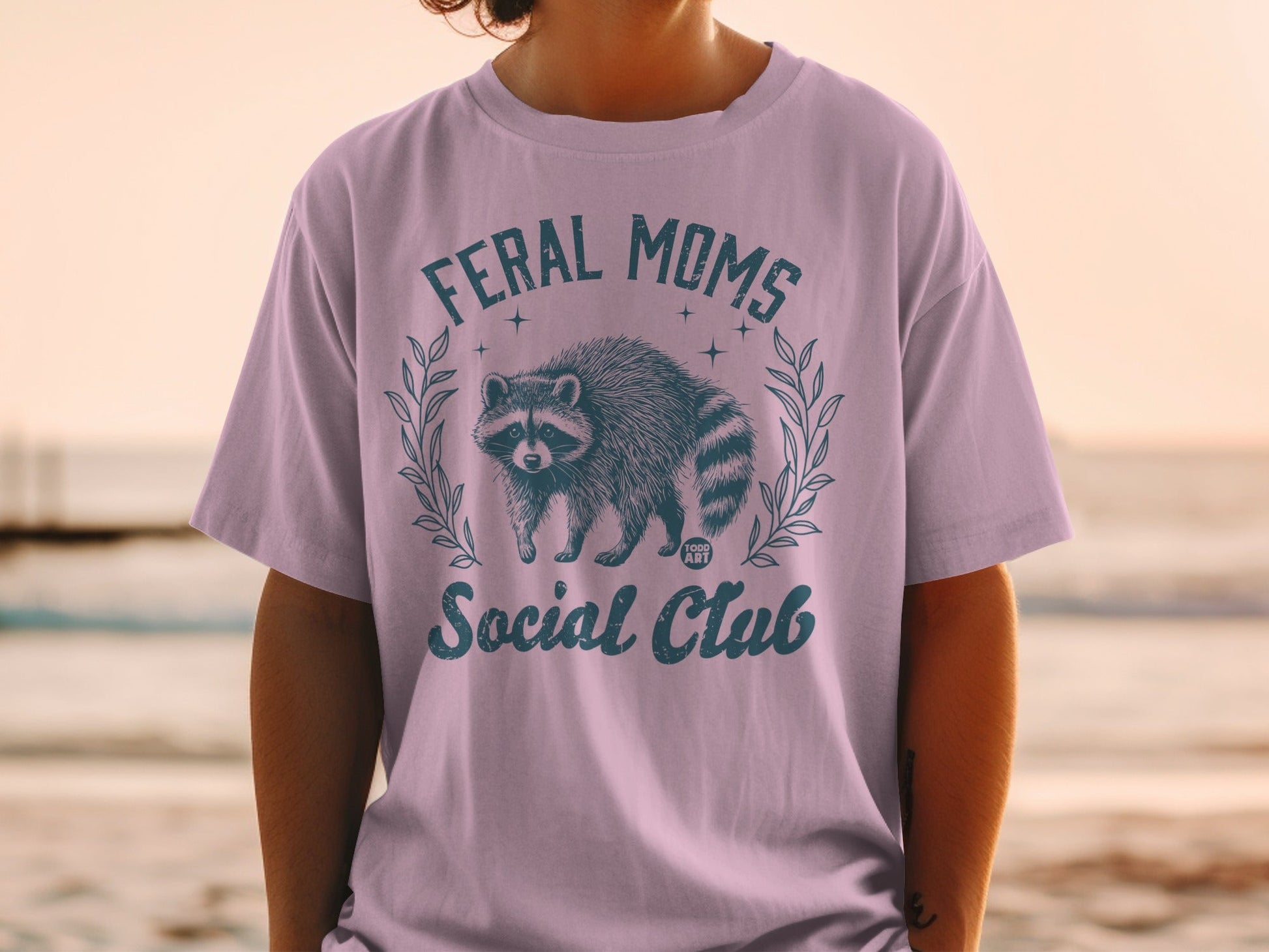 T-shirt with "Feral Moms Social Club" text and a raccoon graphic.
