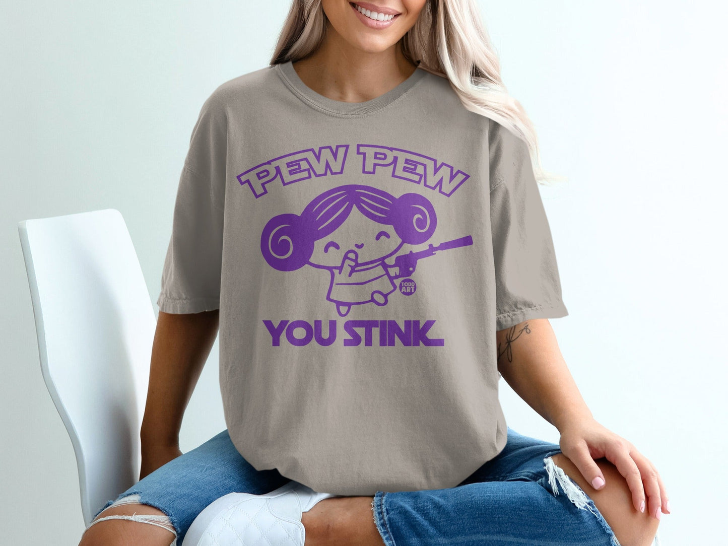 Purple cartoon girl with gun, "Pew Pew You Stink" text, on beige t-shirt.