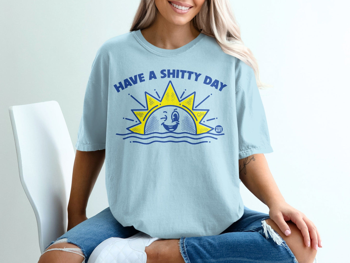 Light blue t-shirt with a sun winking and the text "HAVE A SHITTY DAY".