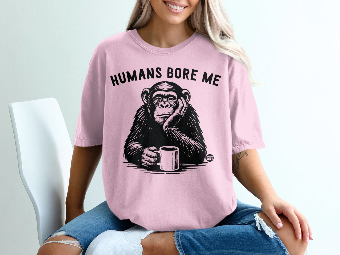 Pink t-shirt with black graphic of chimpanzee holding coffee cup, text "HUMANS BORE ME".