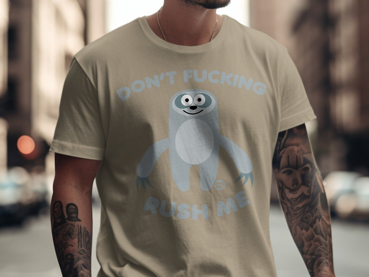 Light blue sloth graphic with "DON'T FUCKING RUSH ME" text on a tan t-shirt.