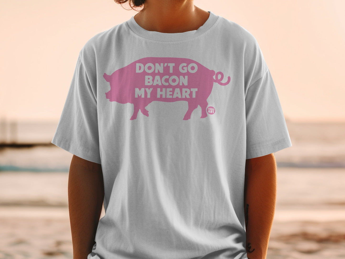 White t-shirt featuring a pink pig silhouette with text "DON'T GO BACON MY HEART".