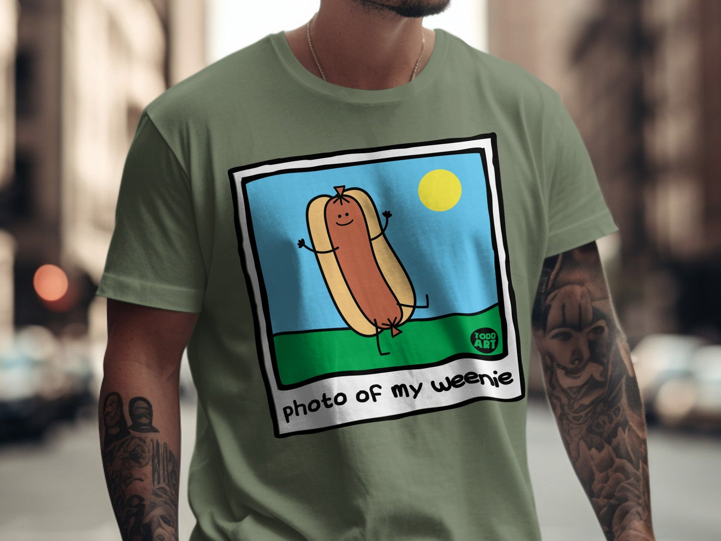 Cartoon hot dog with smiling face and arms, on green t-shirt, with "photo of my weenie" text.