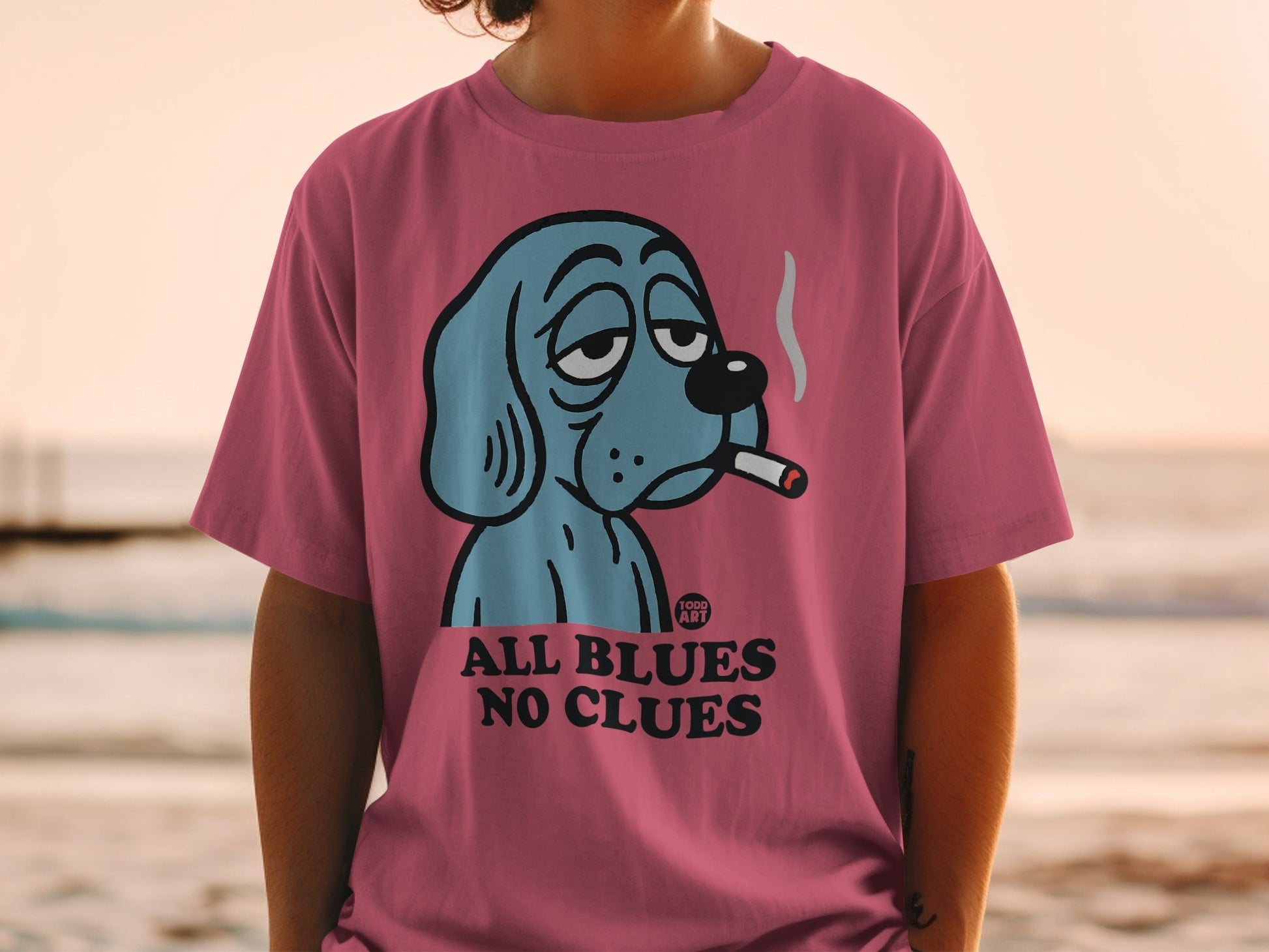 Pink t-shirt with blue cartoon dog smoking, text "ALL BLUES NO CLUES"