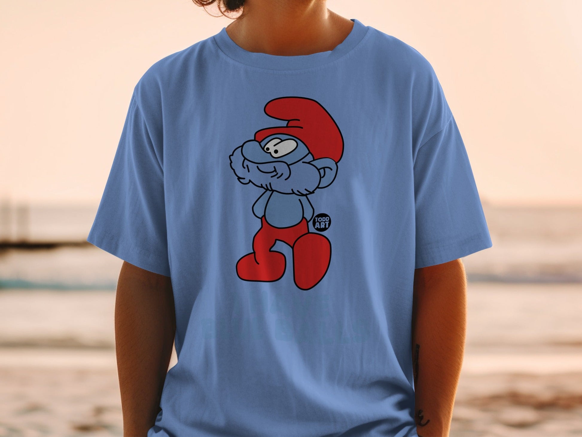 Blue t-shirt with a cartoon illustration of a Smurf in red hat and pants.