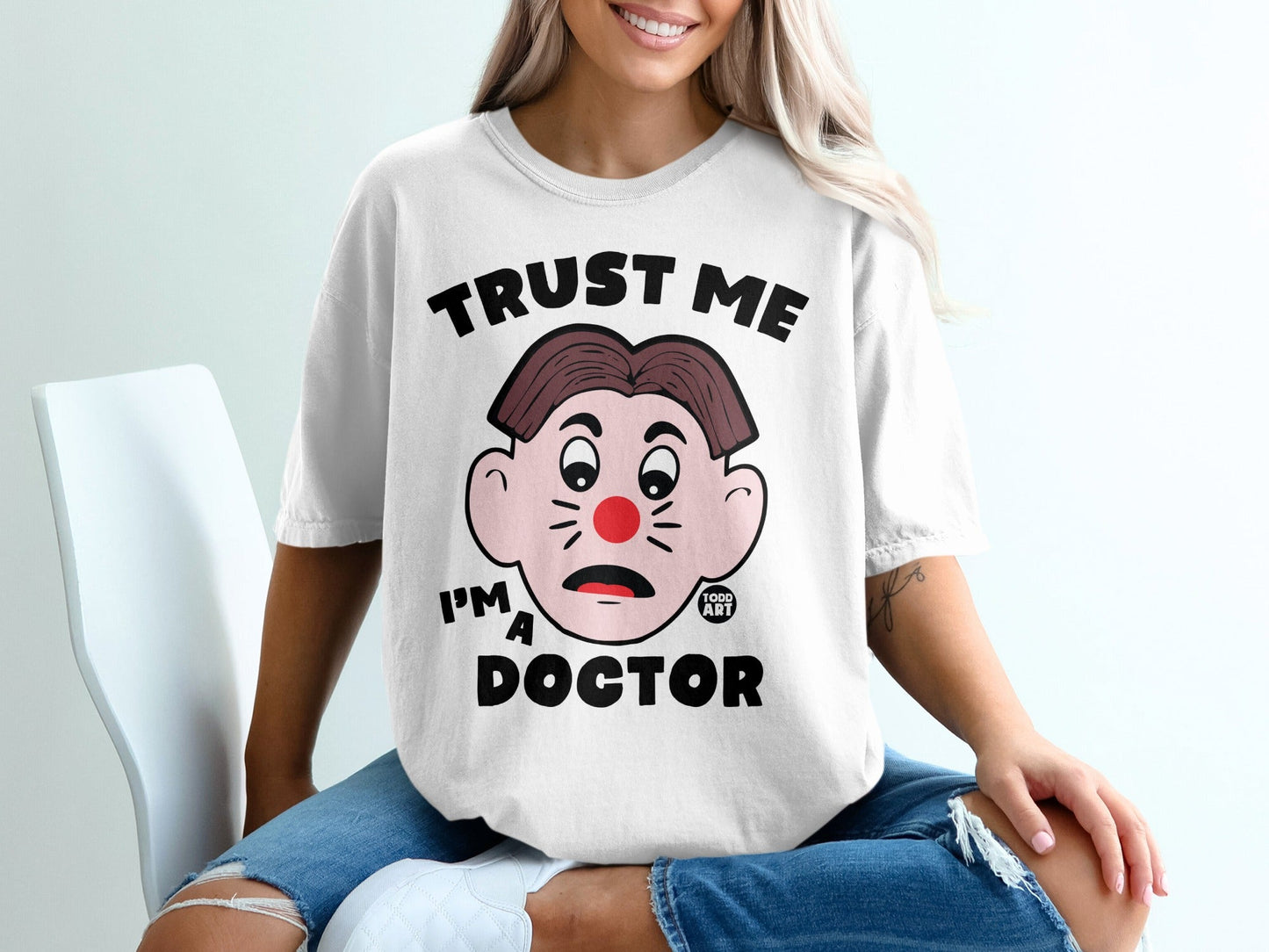 White t-shirt with "TRUST ME I'M A DOCTOR" text and cartoon doctor graphic.