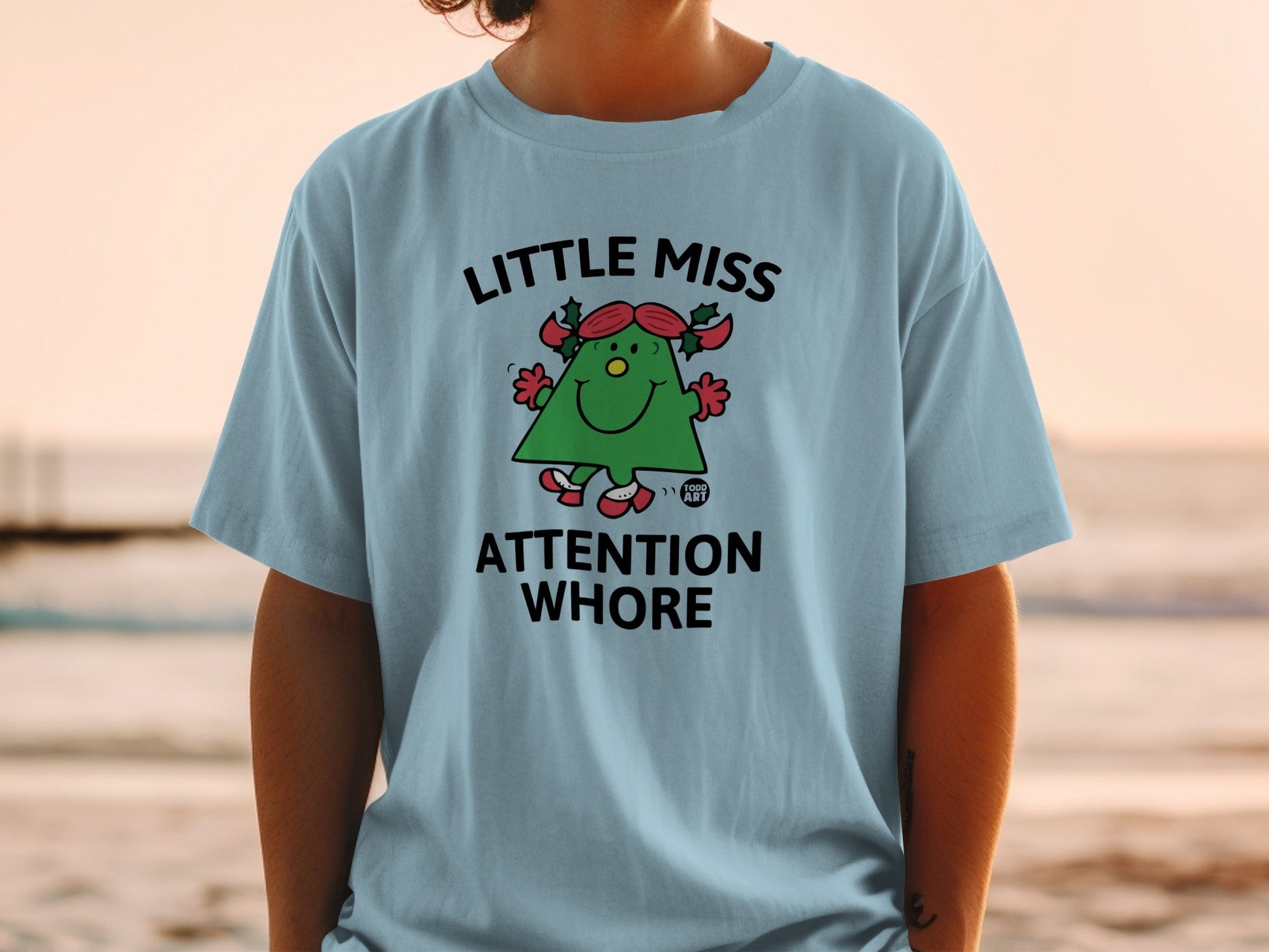 Light blue t-shirt with a cartoon Christmas tree saying "Little Miss Attention Whore".