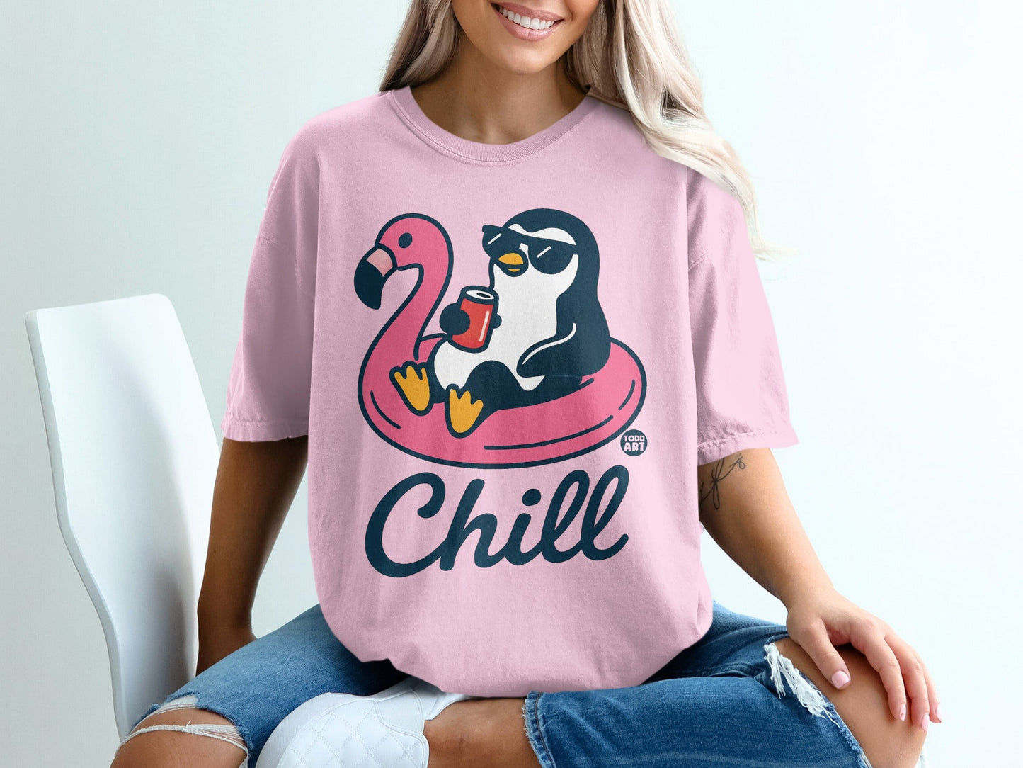 Pink t-shirt with a penguin wearing sunglasses floating on a flamingo pool float, holding a drink, and saying "Chill".