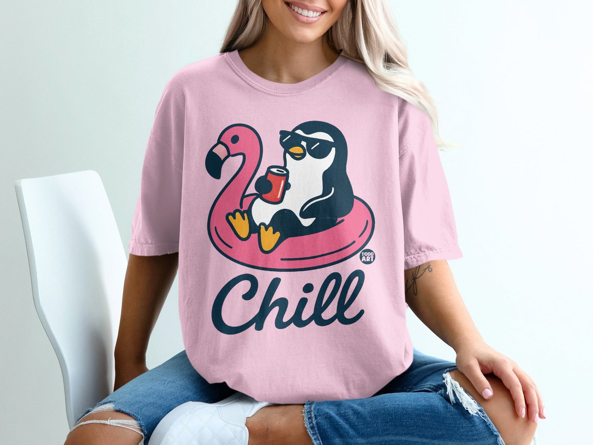 Pink t-shirt with a penguin wearing sunglasses floating on a flamingo pool float, holding a drink, and saying "Chill".