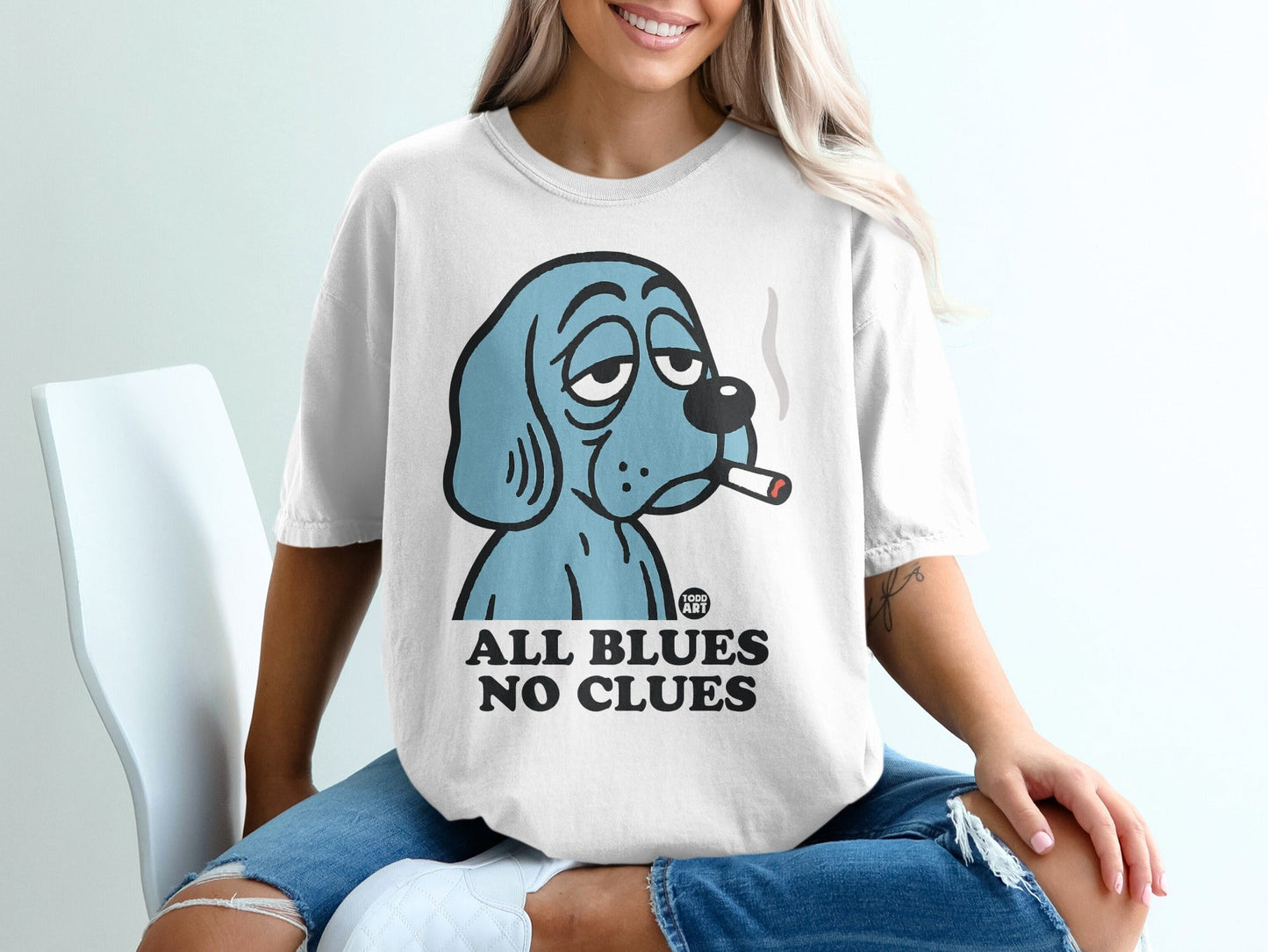 Blue cartoon dog with sad eyes smokes a cigarette on a white t-shirt.