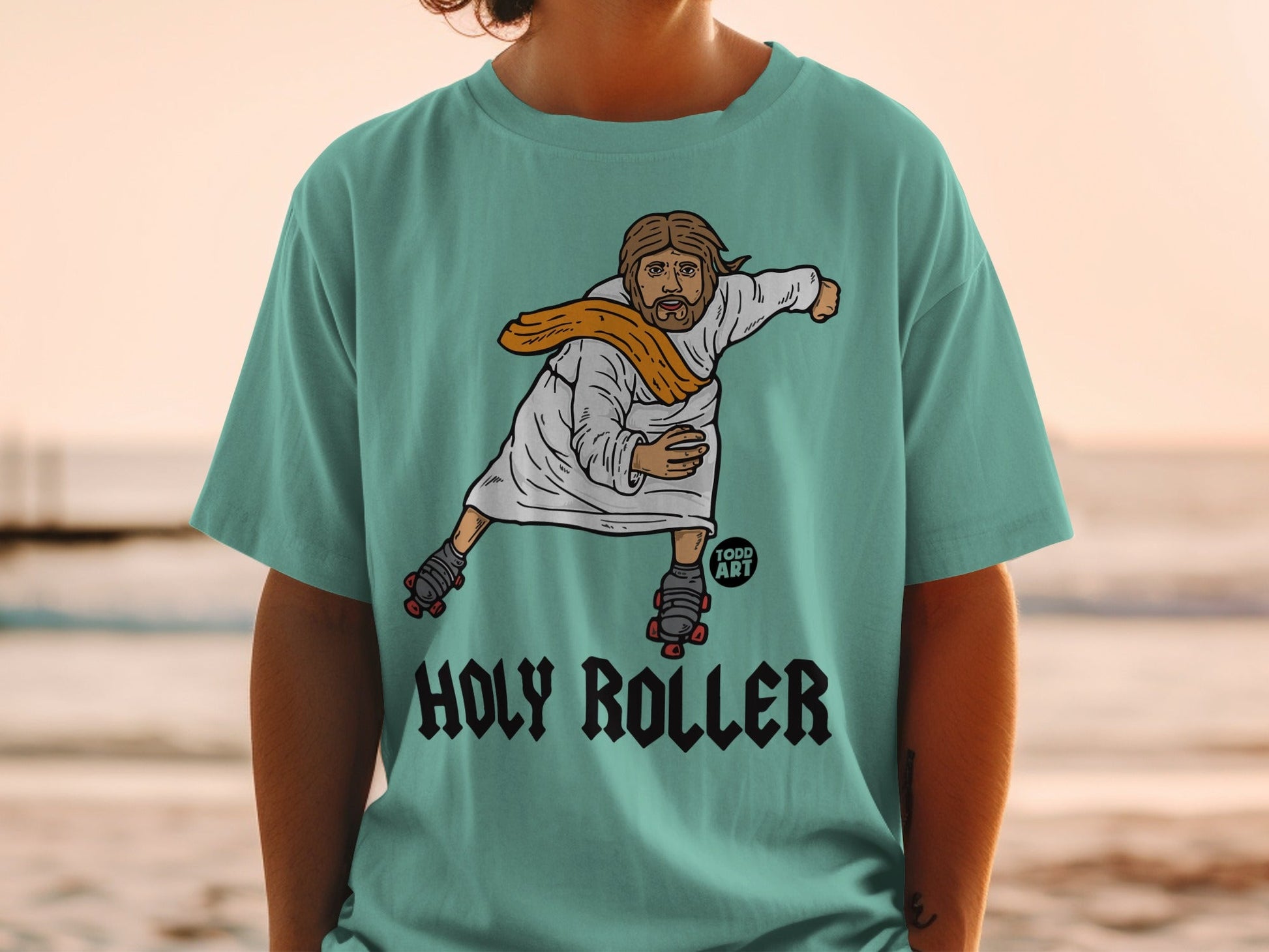 T-shirt with Jesus wearing roller skates and a sash, text "HOLY ROLLER".