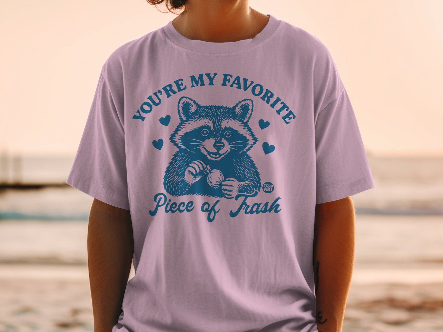 T-shirt with a raccoon holding a heart and the text "YOU'RE MY FAVORITE Piece of Trash".