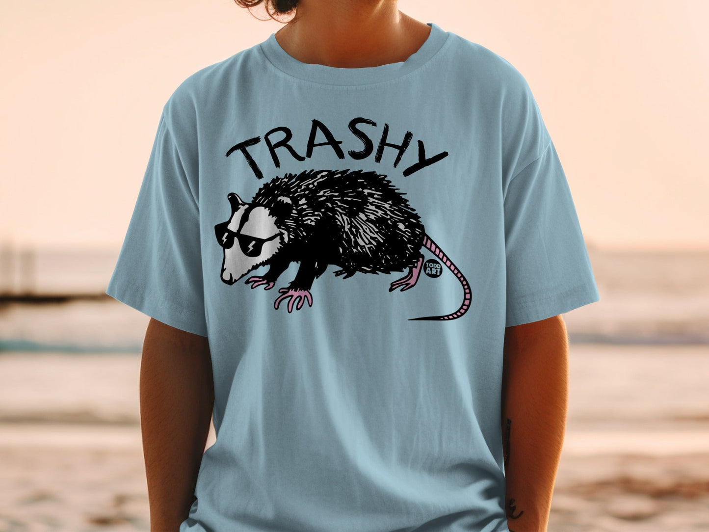 Opossum wearing sunglasses and a t-shirt with "TRASHY" text.