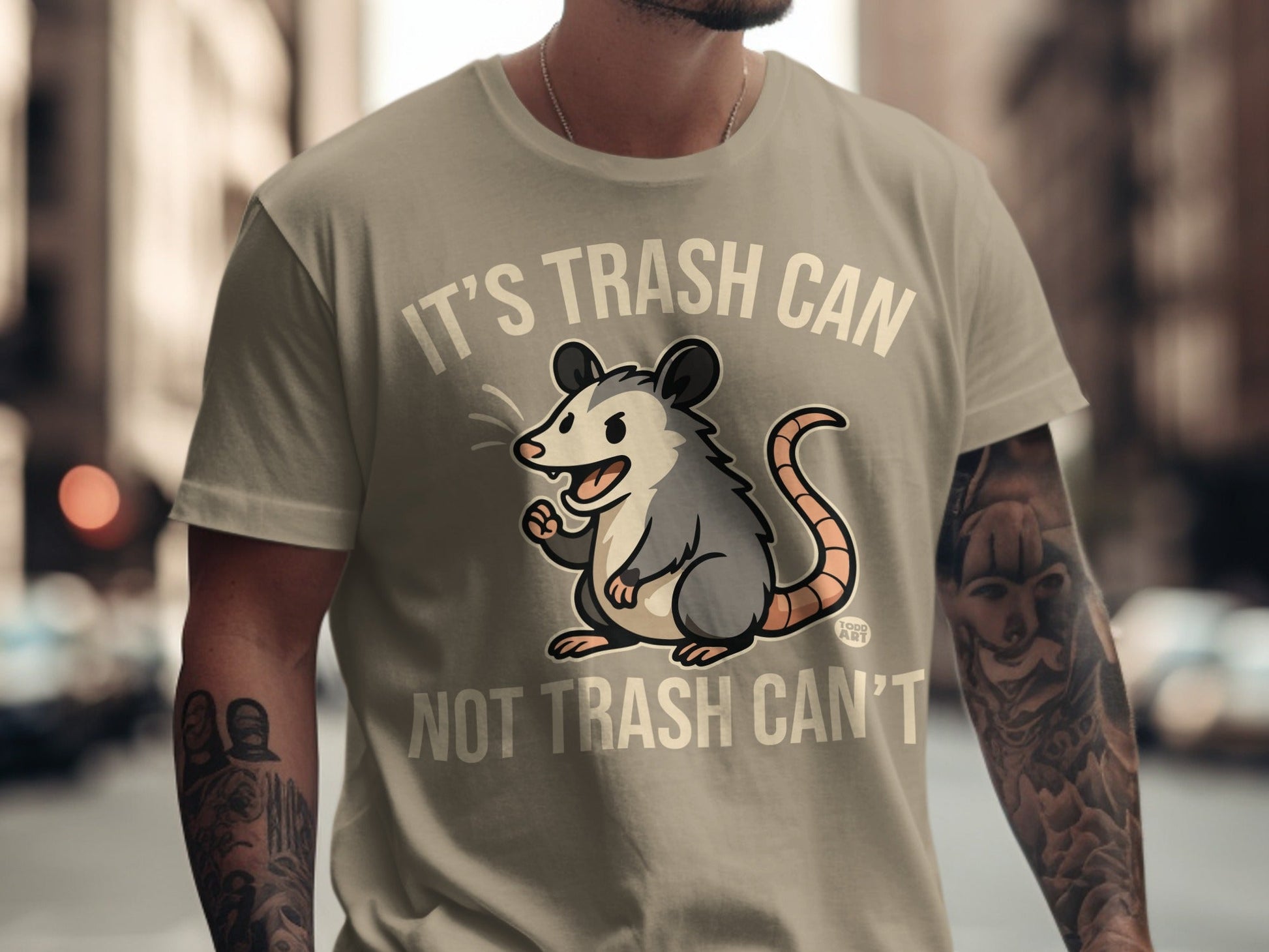 Opossum graphic on a tan t-shirt that reads "It's trash can not trash can't".