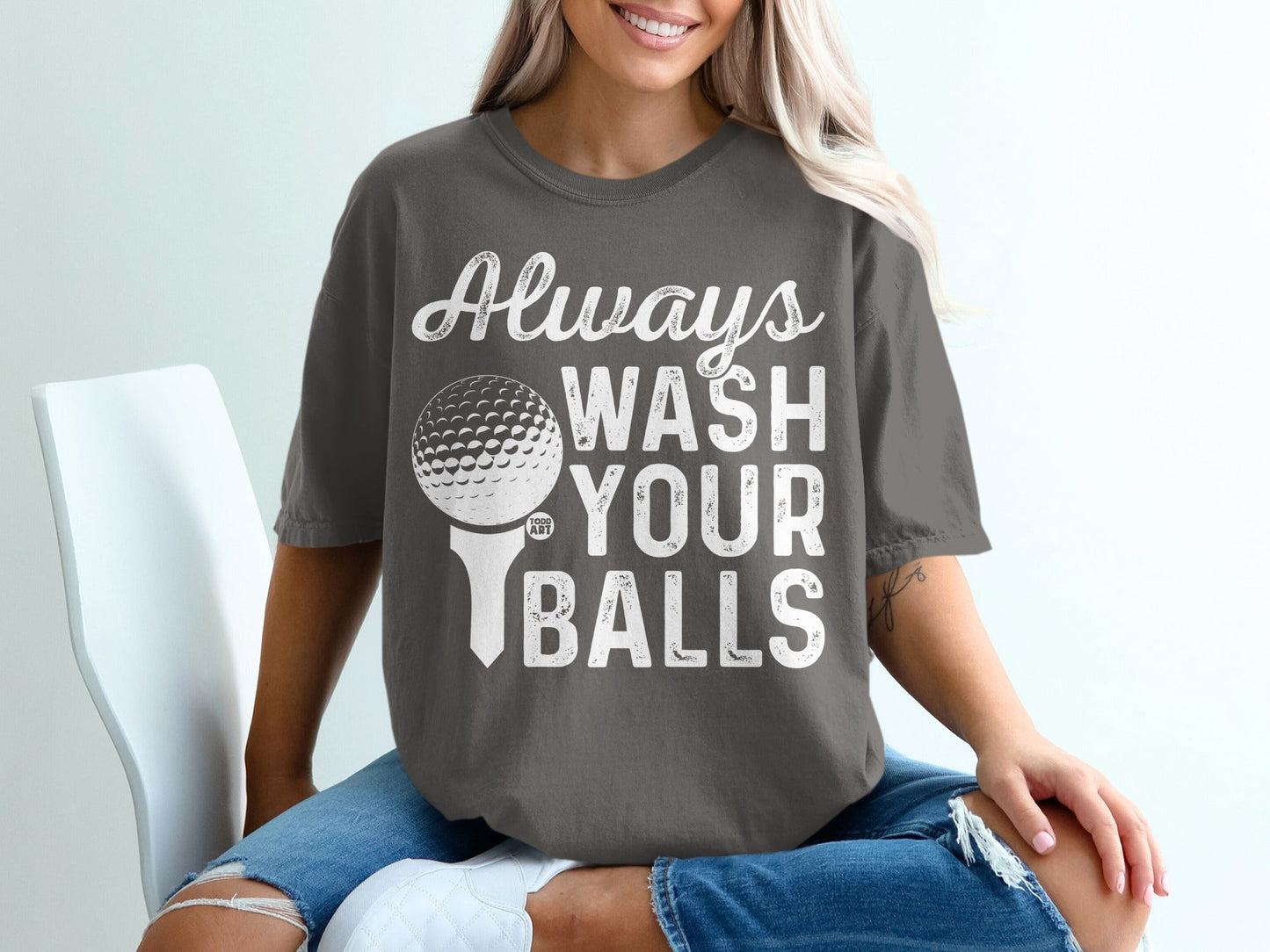 Woman in t-shirt with text "Always WASH YOUR BALLS" and a golf ball on a tee.