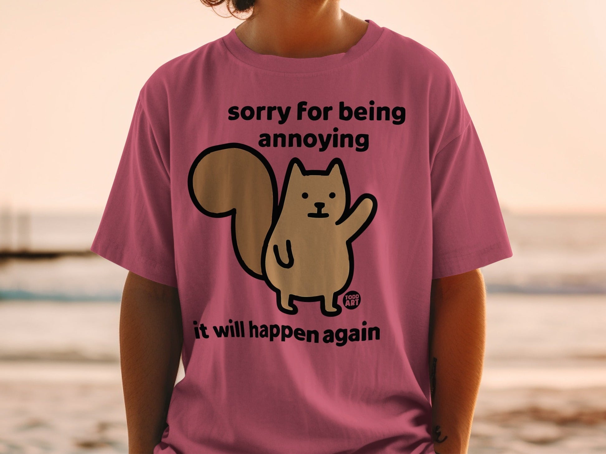 Pink t-shirt with a squirrel graphic and text "sorry for being annoying it will happen again".