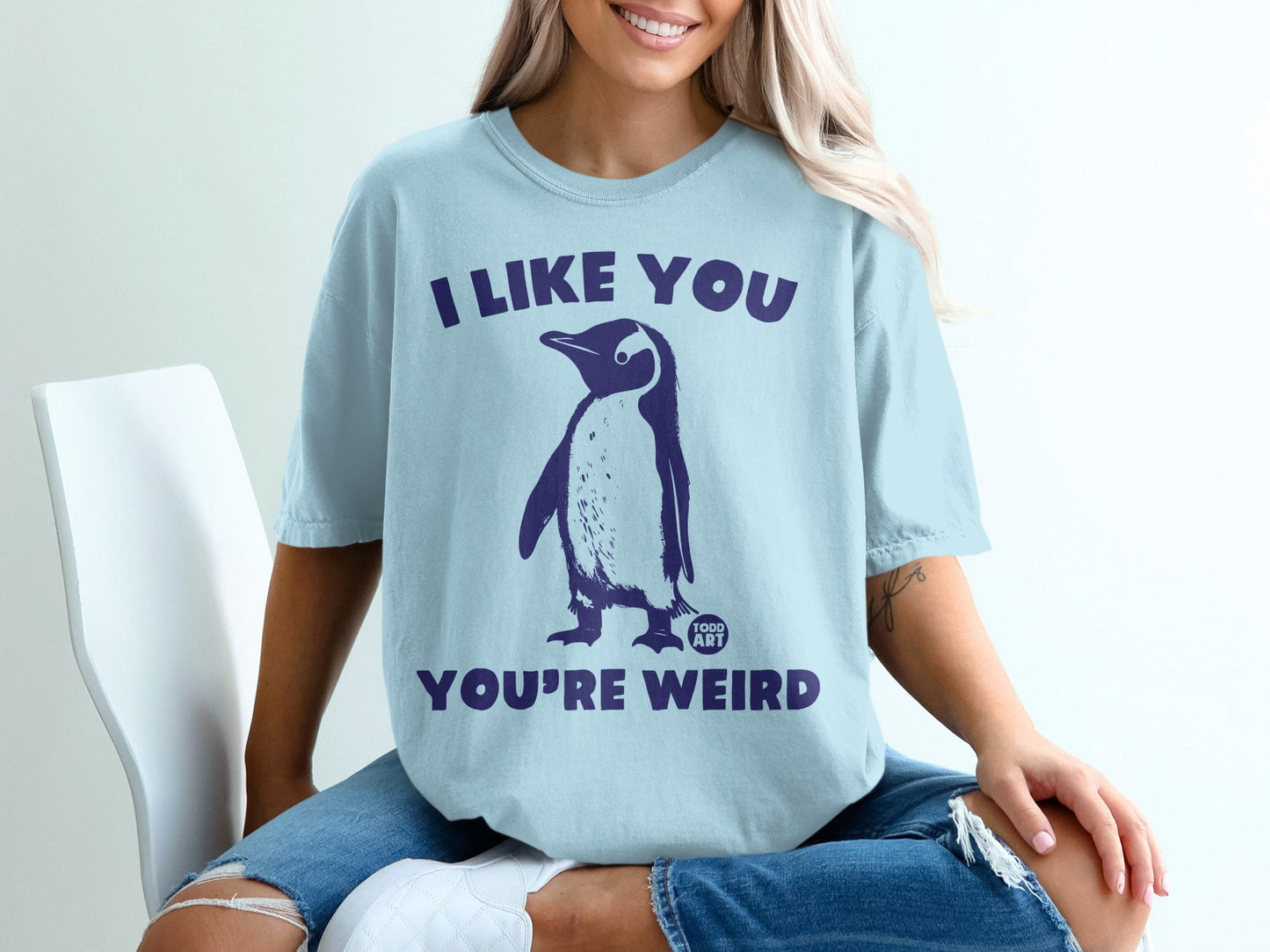 Light blue t-shirt with a penguin graphic and text "I LIKE YOU YOU'RE WEIRD".