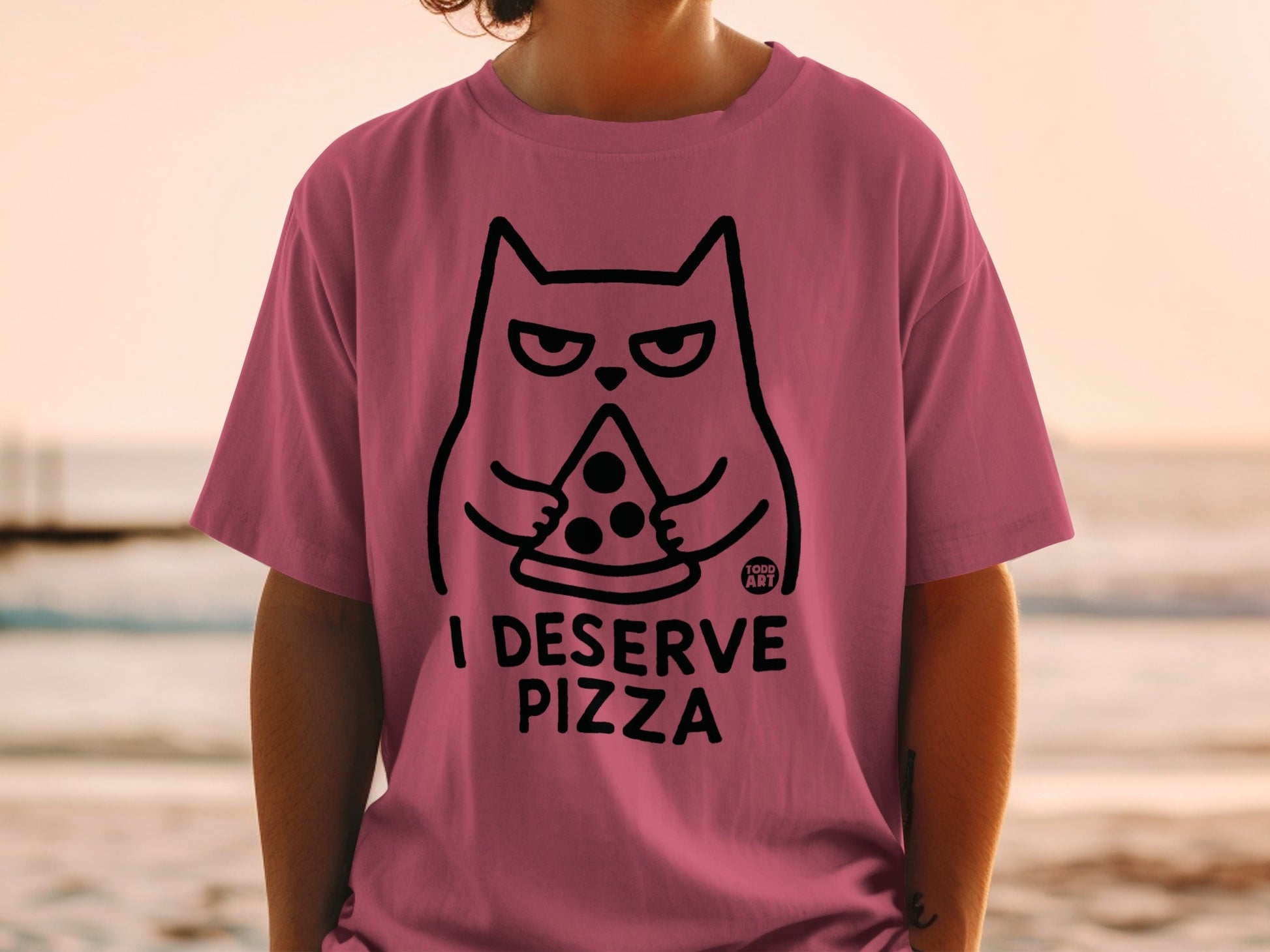 Pink t-shirt with a cartoon cat holding a pizza slice and text "I DESERVE PIZZA".