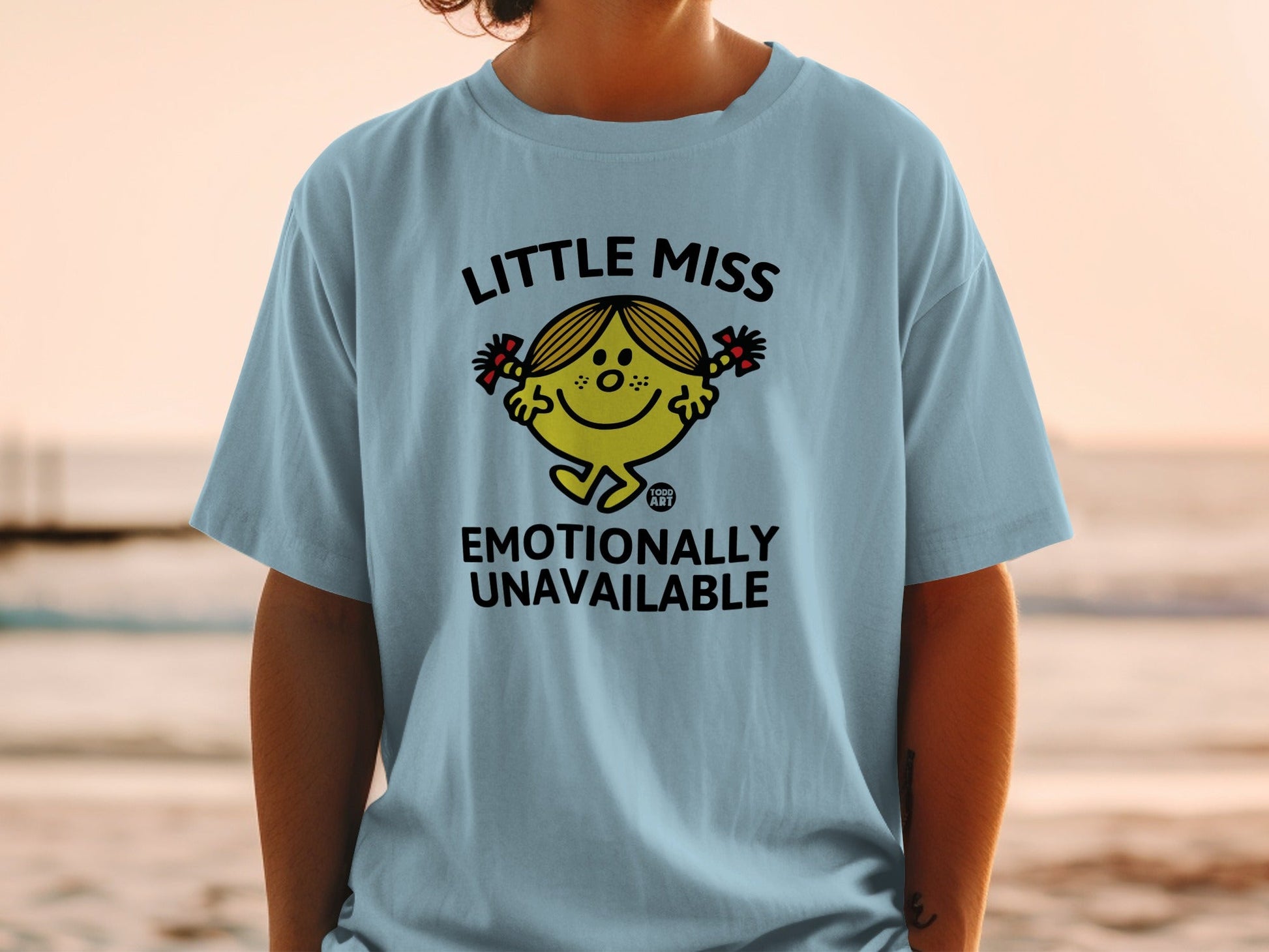 Light blue t-shirt with Little Miss character and "Emotionally Unavailable" text.