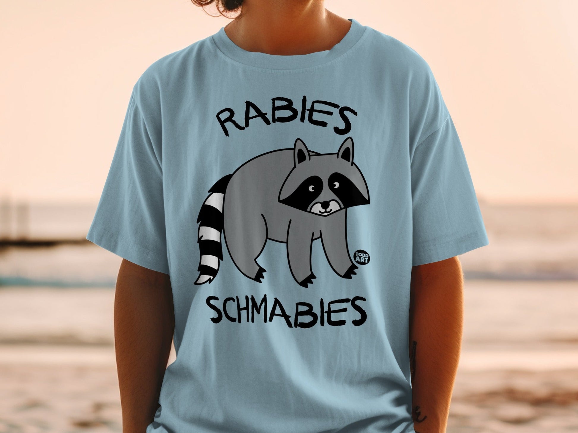 Light blue t-shirt with a cartoon raccoon and text "Rabies Schmabies".