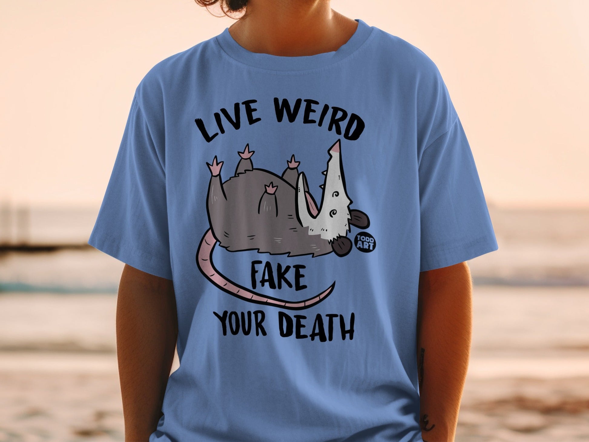 Blue t-shirt with a possum and "Live Weird Fake Your Death" text.
