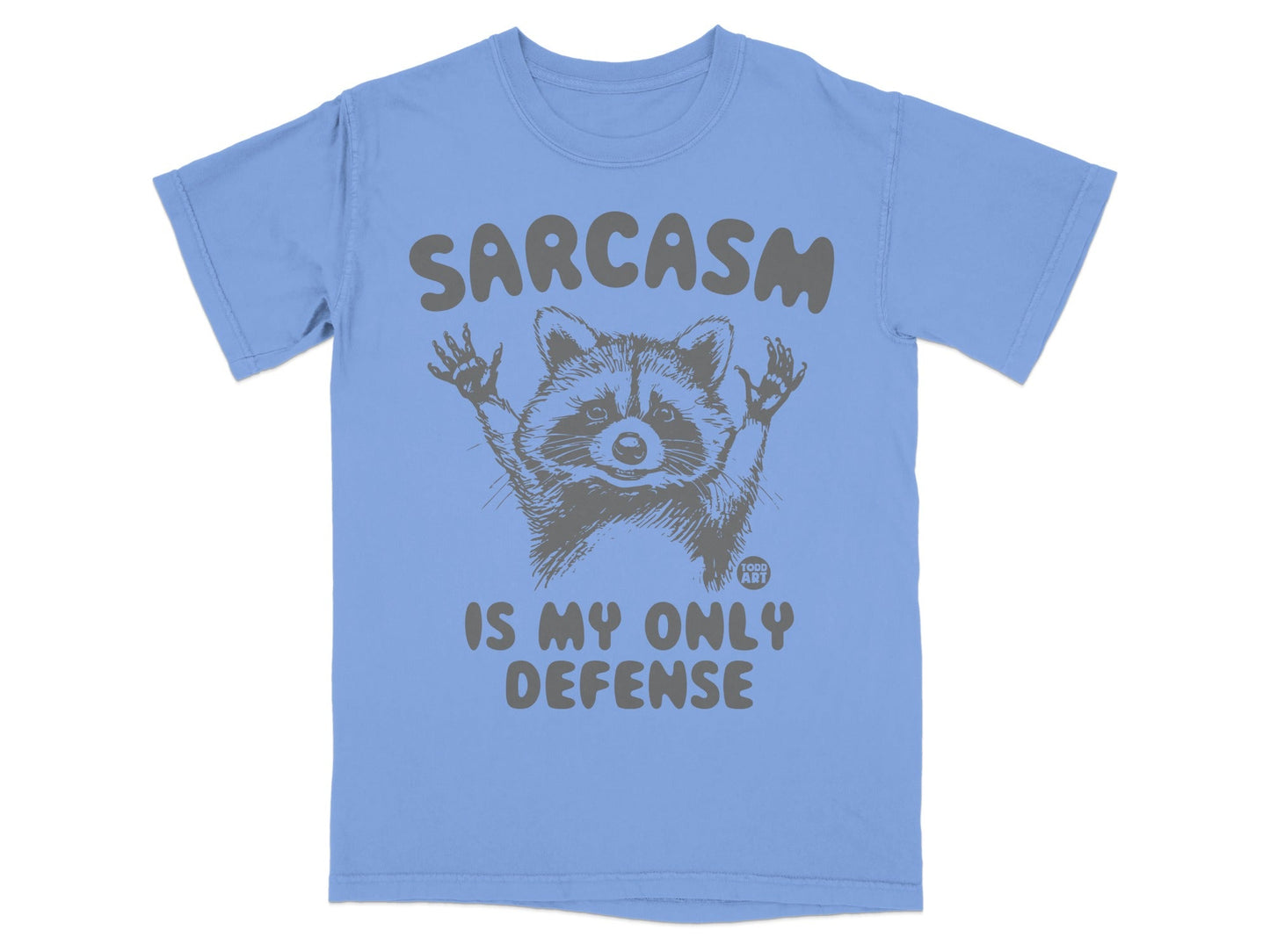Light blue t-shirt with raccoon graphic and "Sarcasm is my only defense" text.