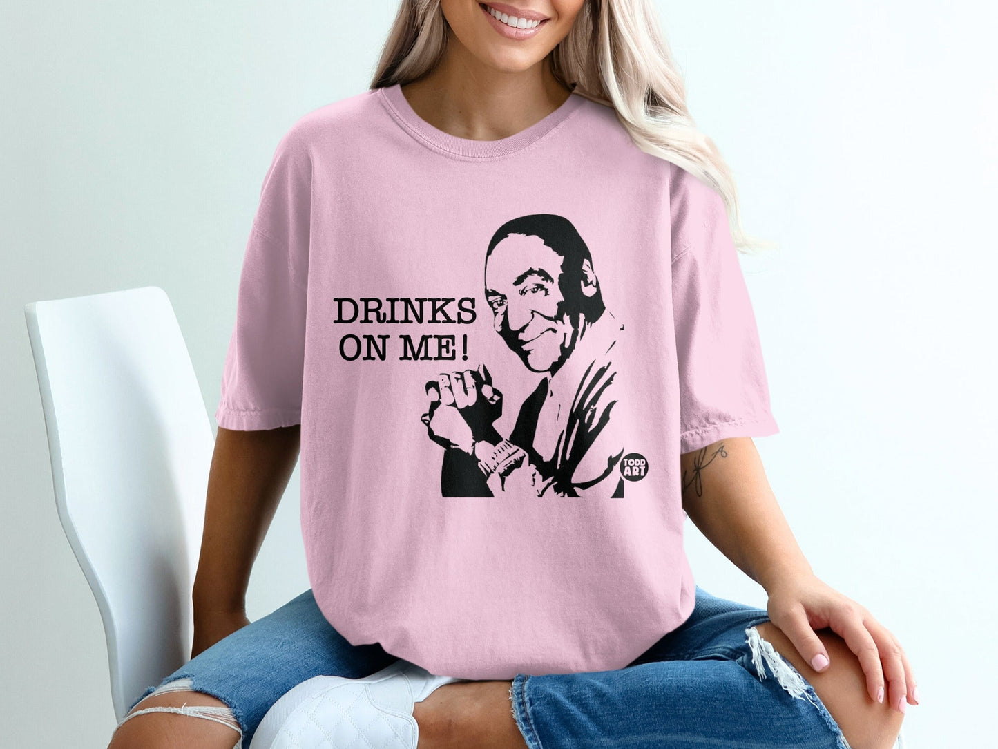 Pink t-shirt with black graphic of a man's face and text "DRINKS ON ME!".