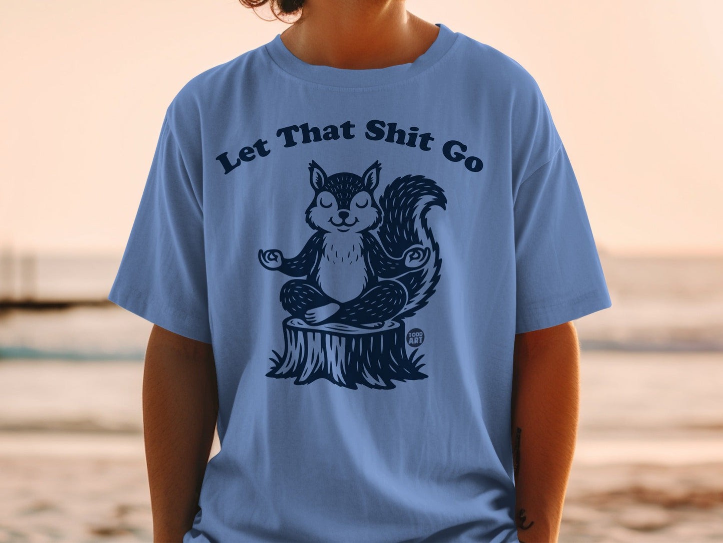 T-shirt with illustration of a meditating squirrel on a tree stump, text "Let That Shit Go".