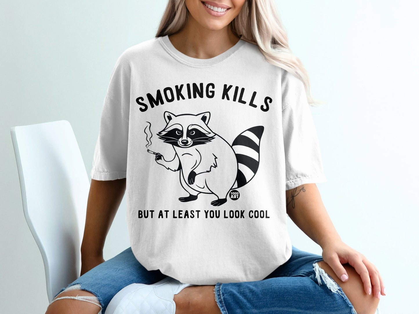 White t-shirt with raccoon graphic and text "Smoking kills but at least you look cool".