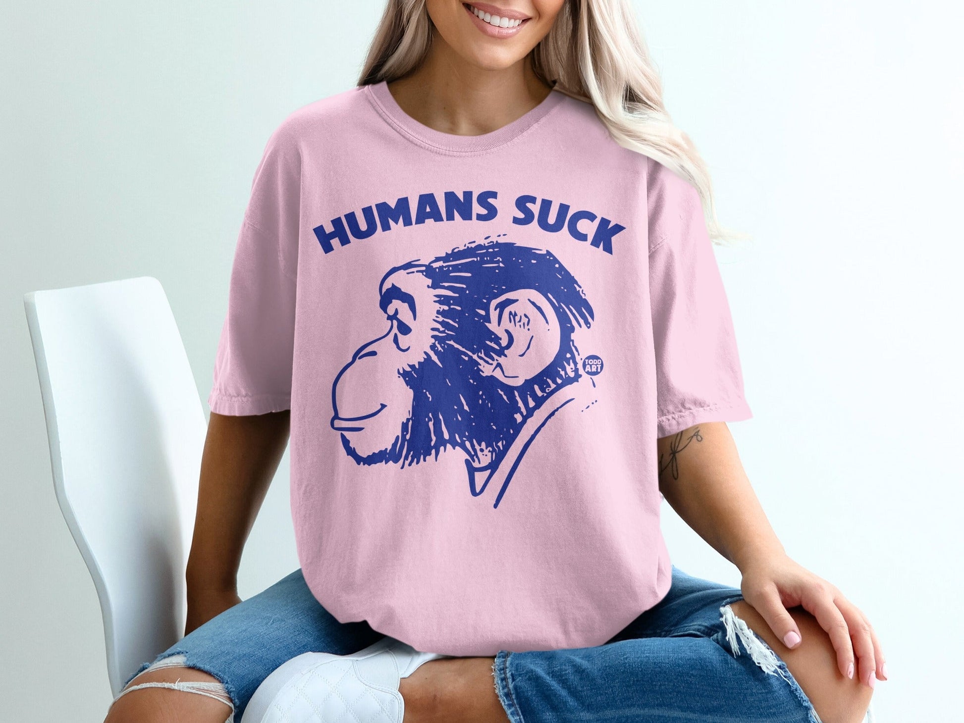 Pink t-shirt with blue graphic of a monkey and text "HUMANS SUCK".