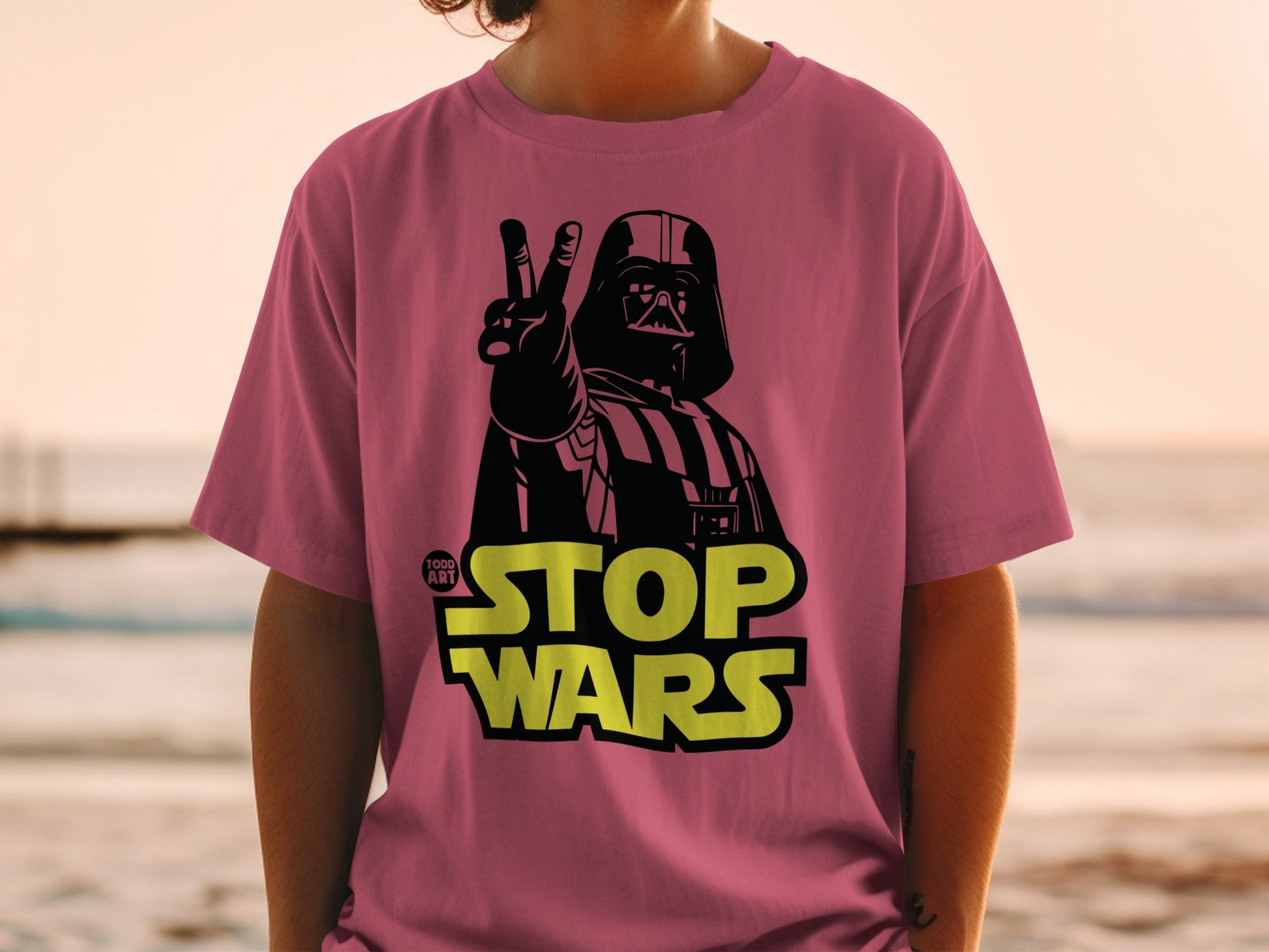 Darth Vader giving peace sign on pink t-shirt with "STOP WARS" text.
