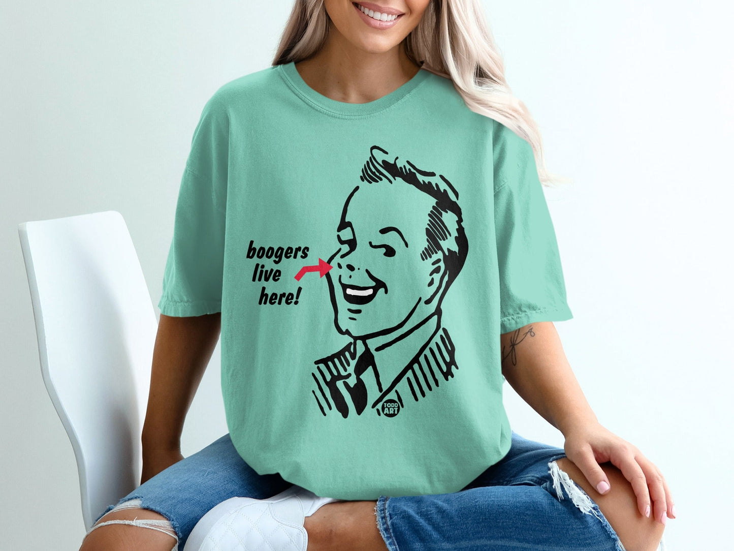 Mint t-shirt featuring a retro cartoon man with a red arrow pointing to his nose that says "boogers live here".