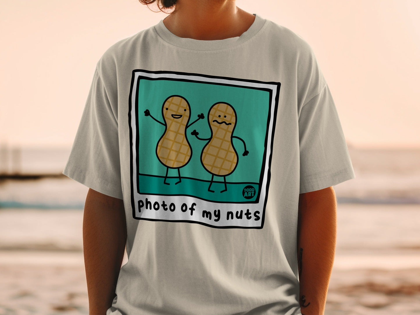Two cartoon peanuts with arms raised, smiling, on a shirt that says "photo of my nuts".