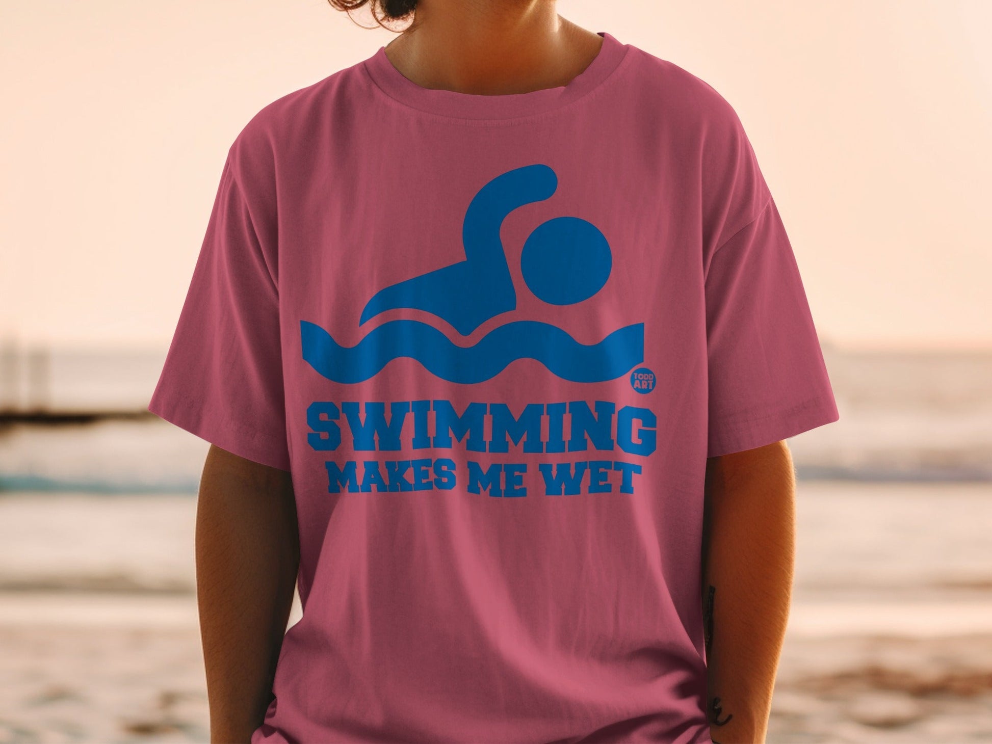 Pink t-shirt with blue swimming graphic and text "SWIMMING MAKES ME WET".