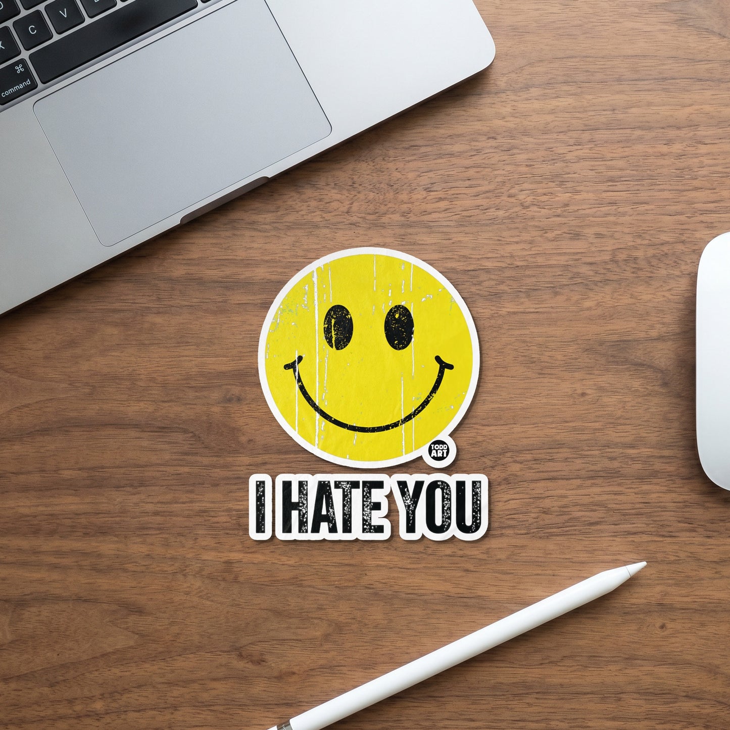 Yellow smiley face sticker with text "I HATE YOU" on a wooden surface.
