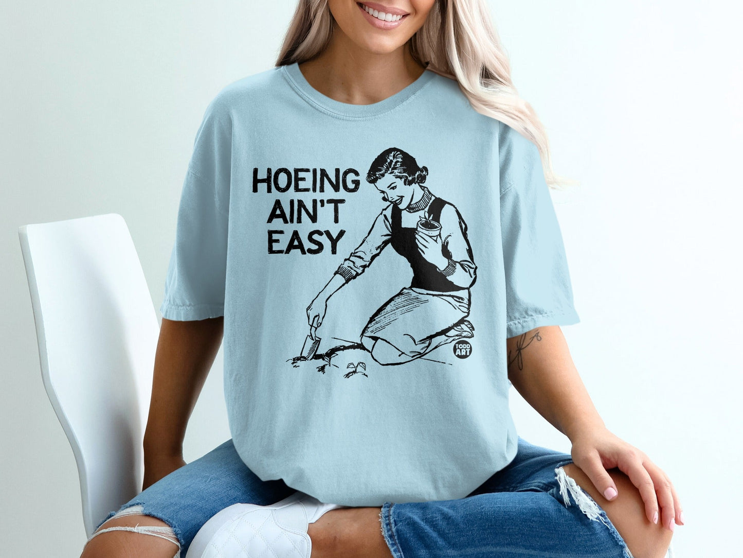 Light blue t-shirt with vintage illustration of a woman gardening and text "Hoeing ain't easy".