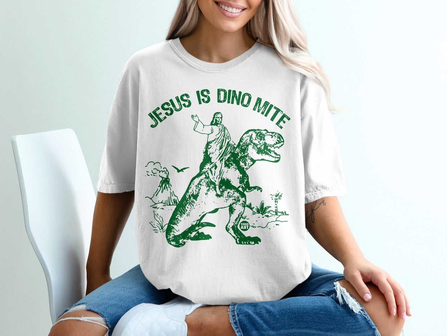 Jesus is Dino Mite text on t-shirt with Jesus riding a dinosaur.