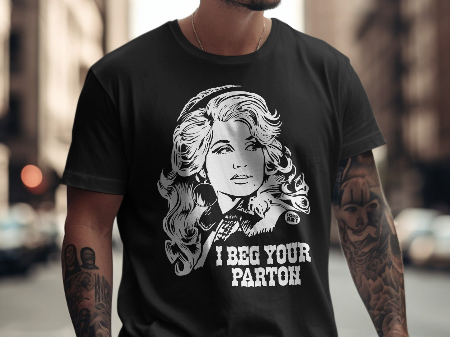 Black t-shirt with white graphic of Dolly Parton and "I BEG YOUR PARTON" text.