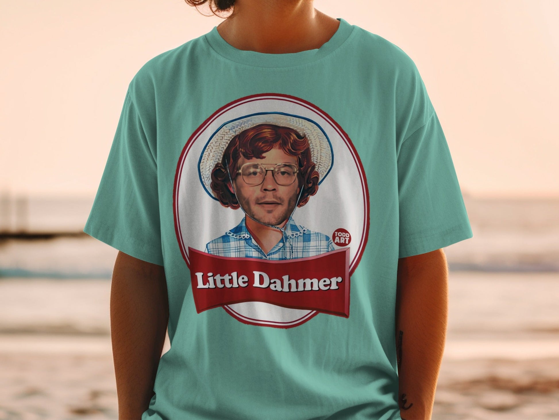 Blue t-shirt with graphic of man in hat and checkered shirt, "Little Dahmer" text.