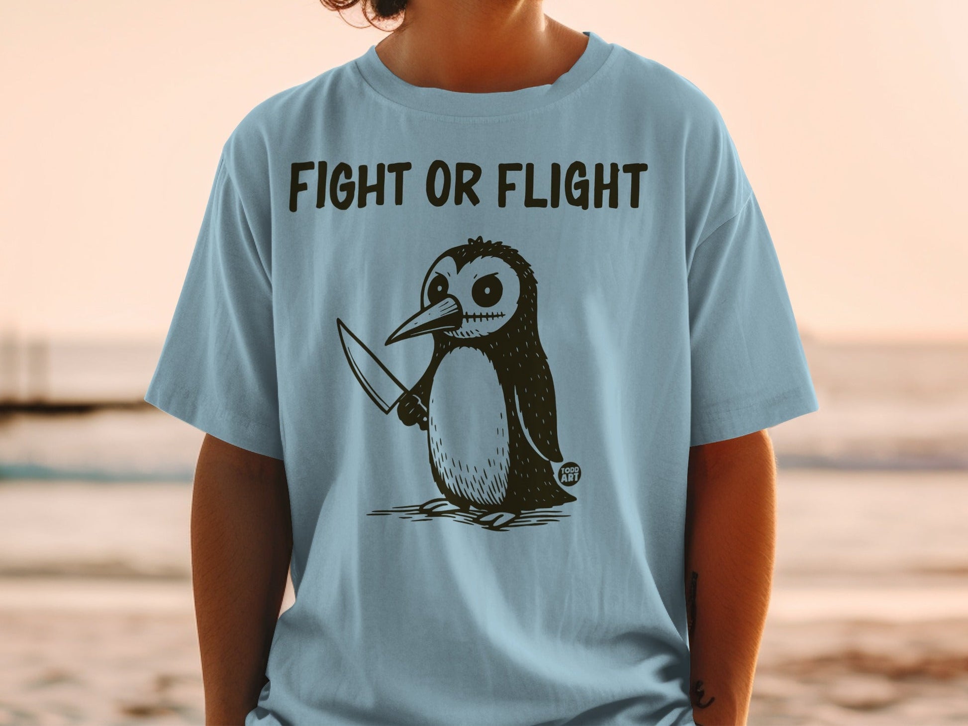 Light blue t-shirt with cartoon penguin holding a knife, text reads "FIGHT OR FLIGHT".