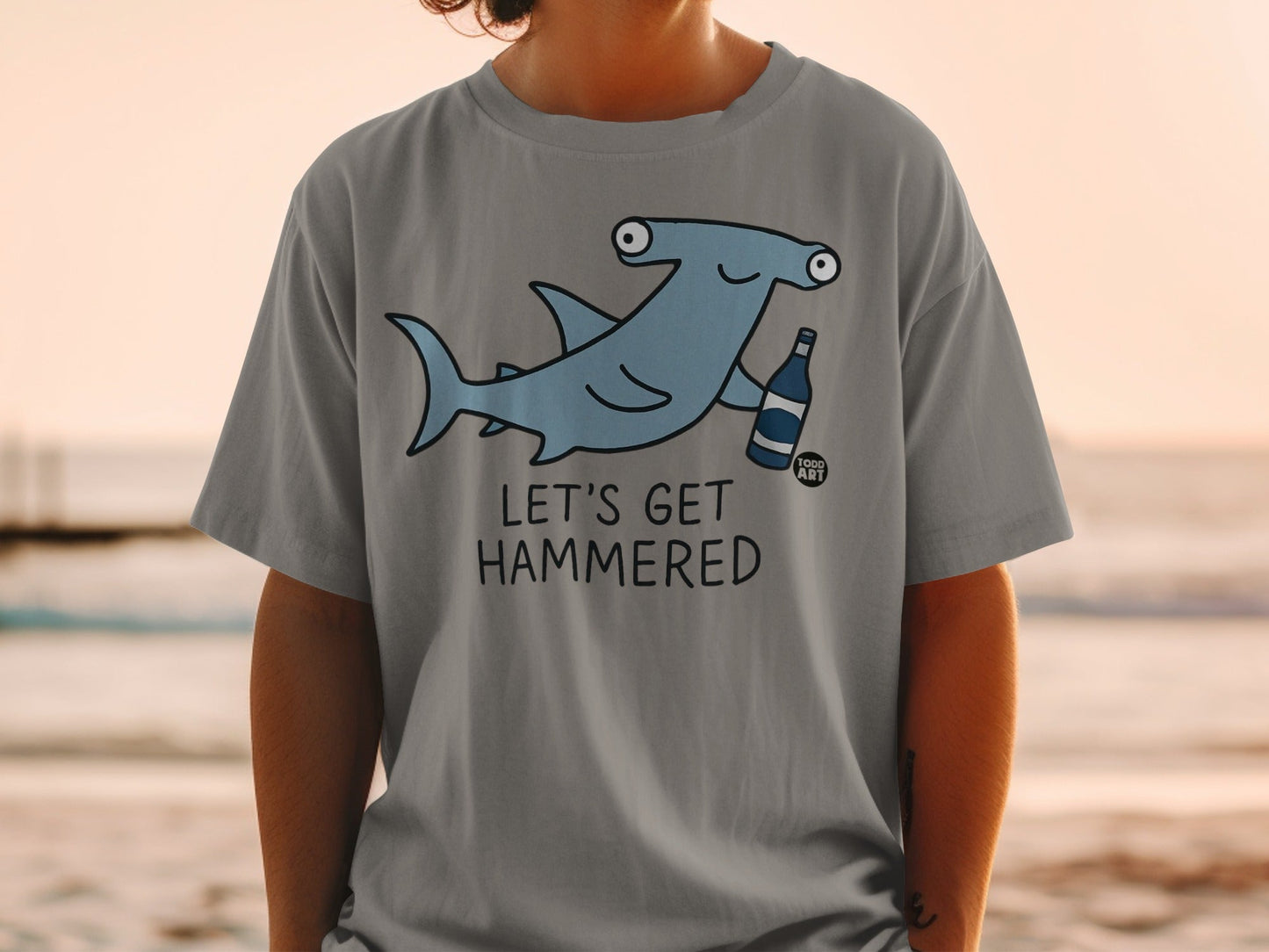 Grey t-shirt with cartoon hammerhead shark holding a beer bottle, text reads "Let's Get Hammered".