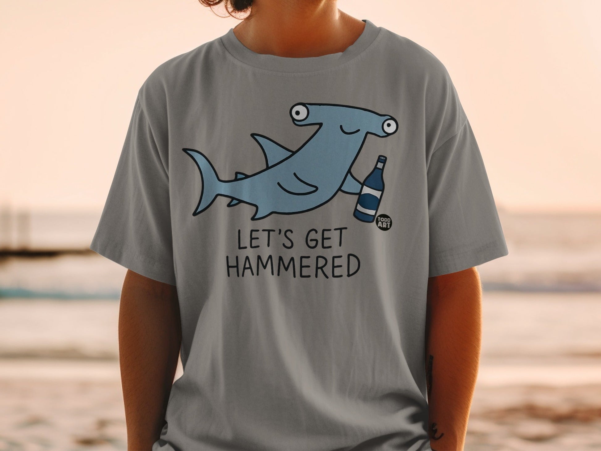 Grey t-shirt with cartoon hammerhead shark holding a beer bottle, text reads "Let's Get Hammered".