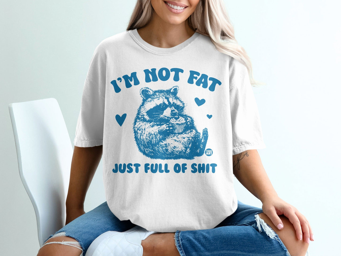 White t-shirt with raccoon holding cupcake and "I'm not fat just full of shit" text.