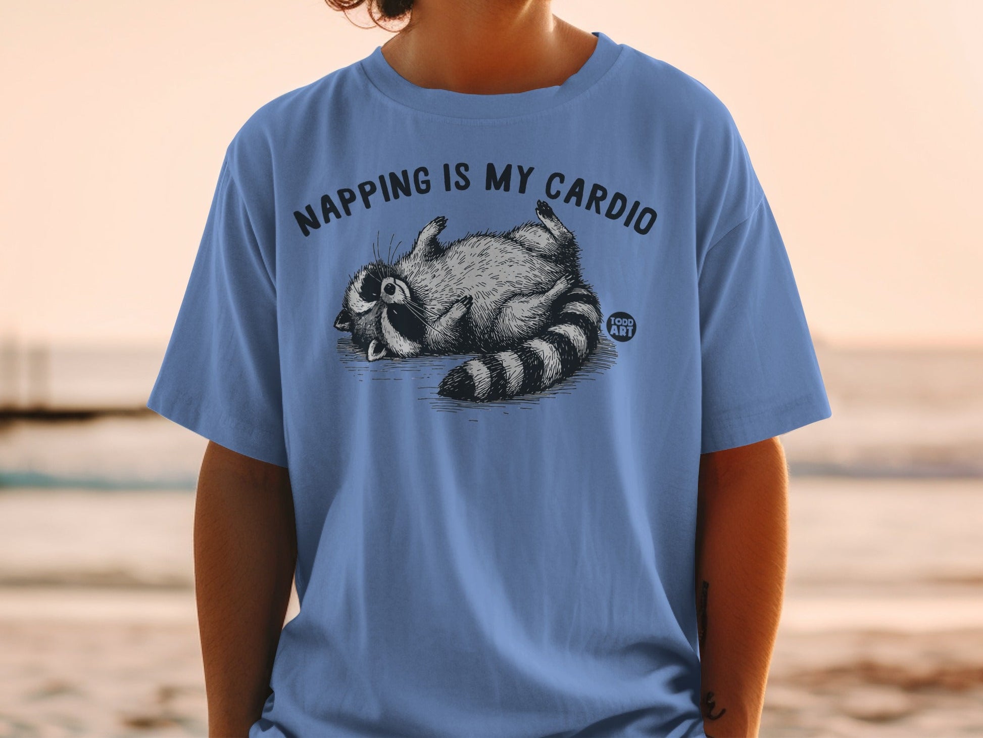 T-shirt with raccoon saying "Napping is my cardio" and "1000 ART" logo.