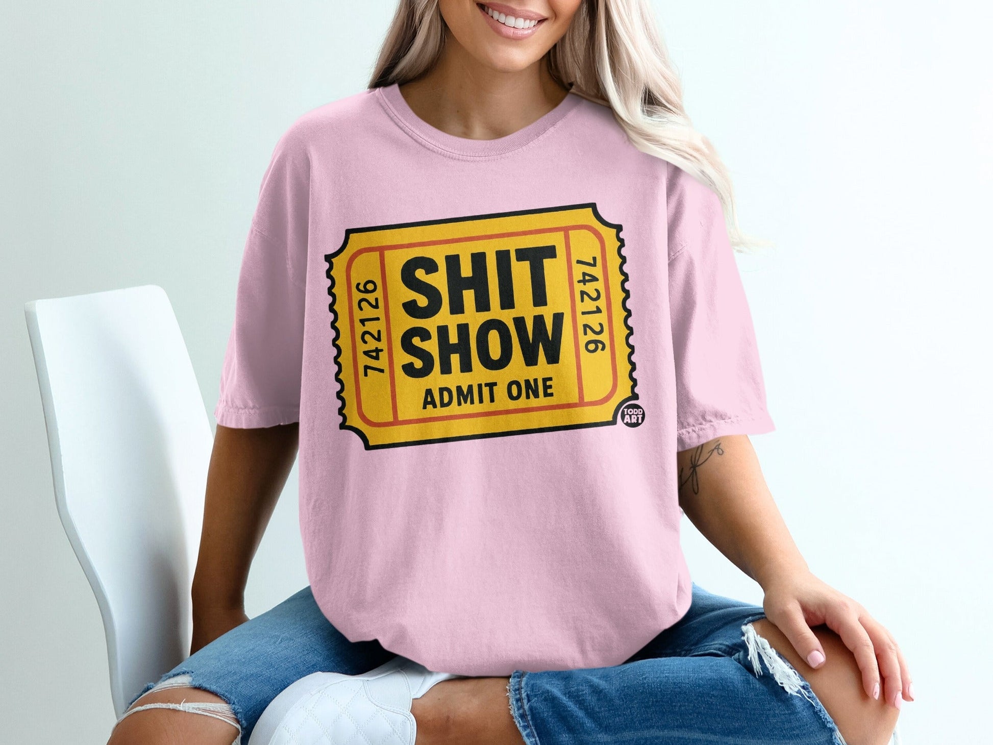 Pink t-shirt with "Shit Show Admit One" ticket graphic.