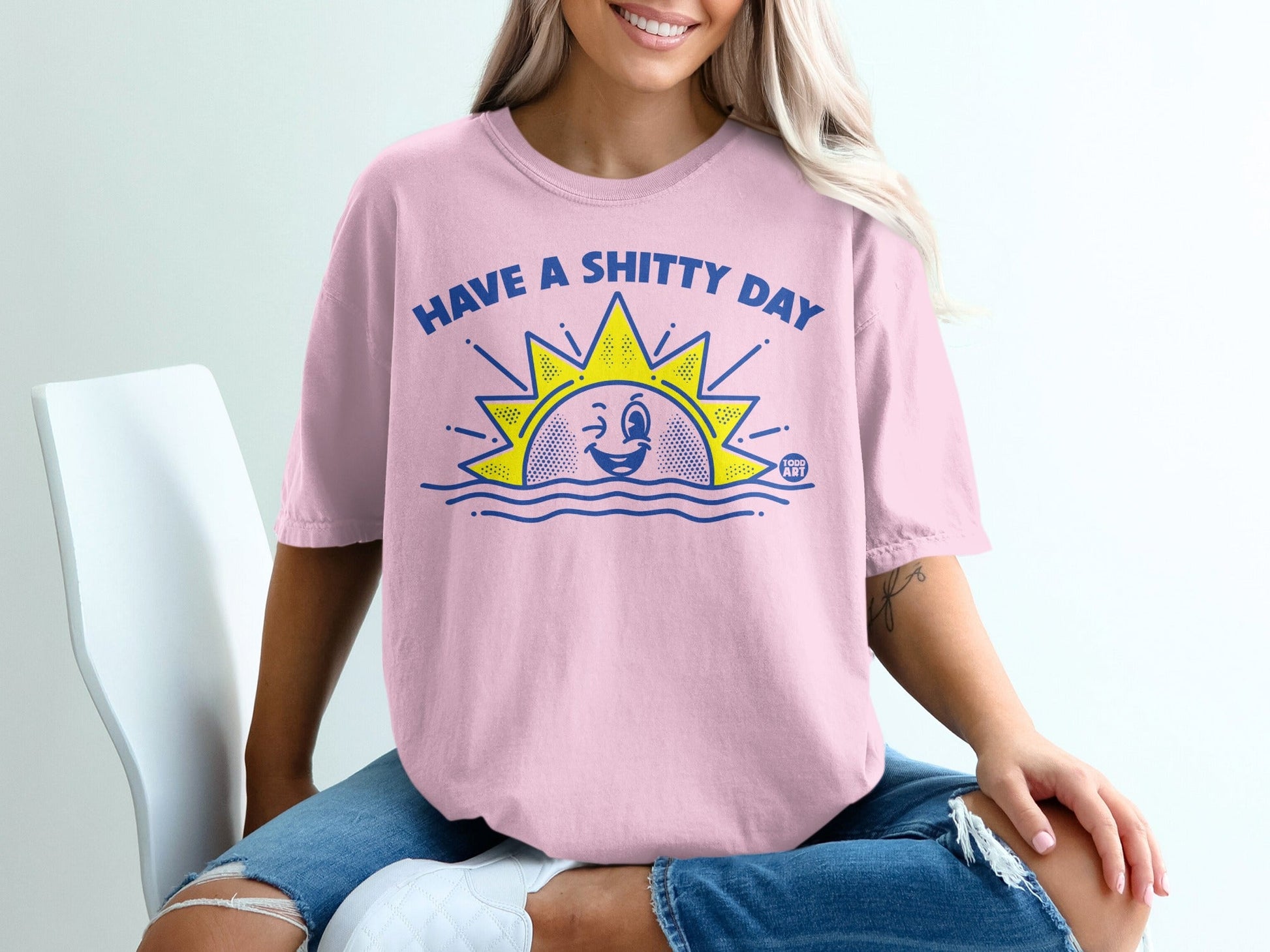 Pink t-shirt with a winking sun graphic saying "HAVE A SHITTY DAY".