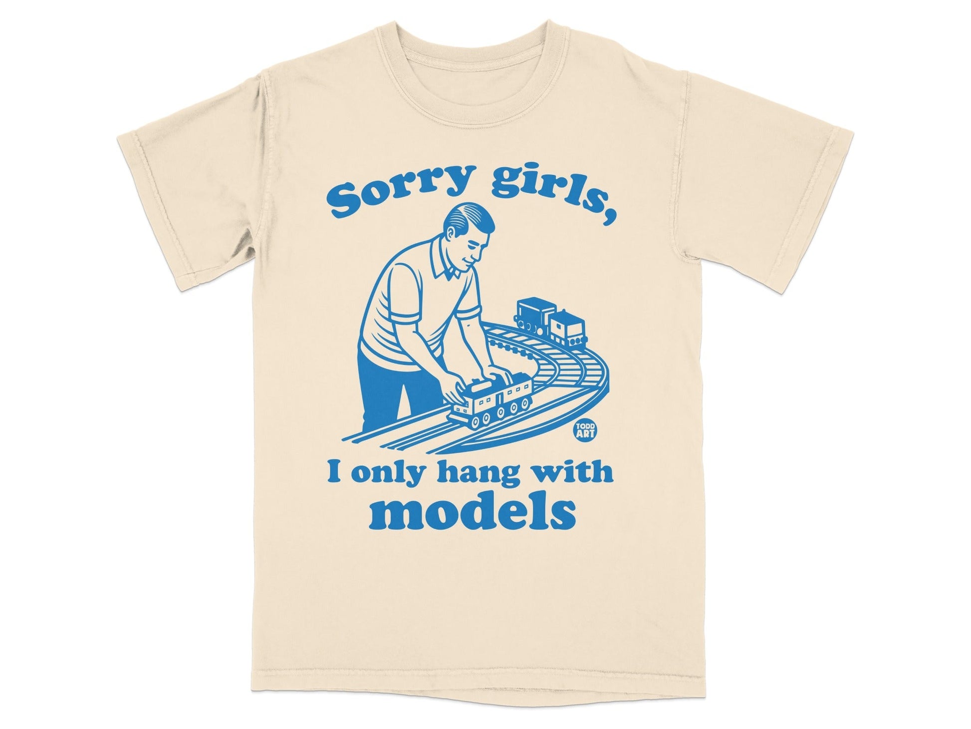 Cream t-shirt with blue graphic: Man playing with toy train set.