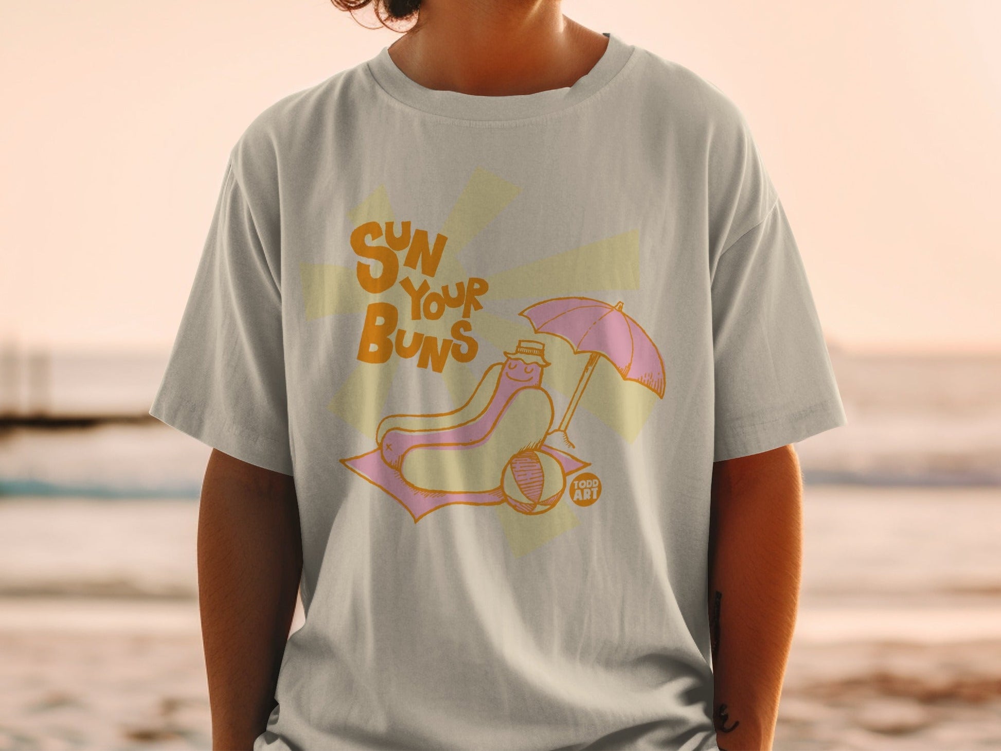 T-shirt with a hot dog under an umbrella and the text "Sun Your Buns".